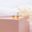 a pair of gold earrings on a pink box